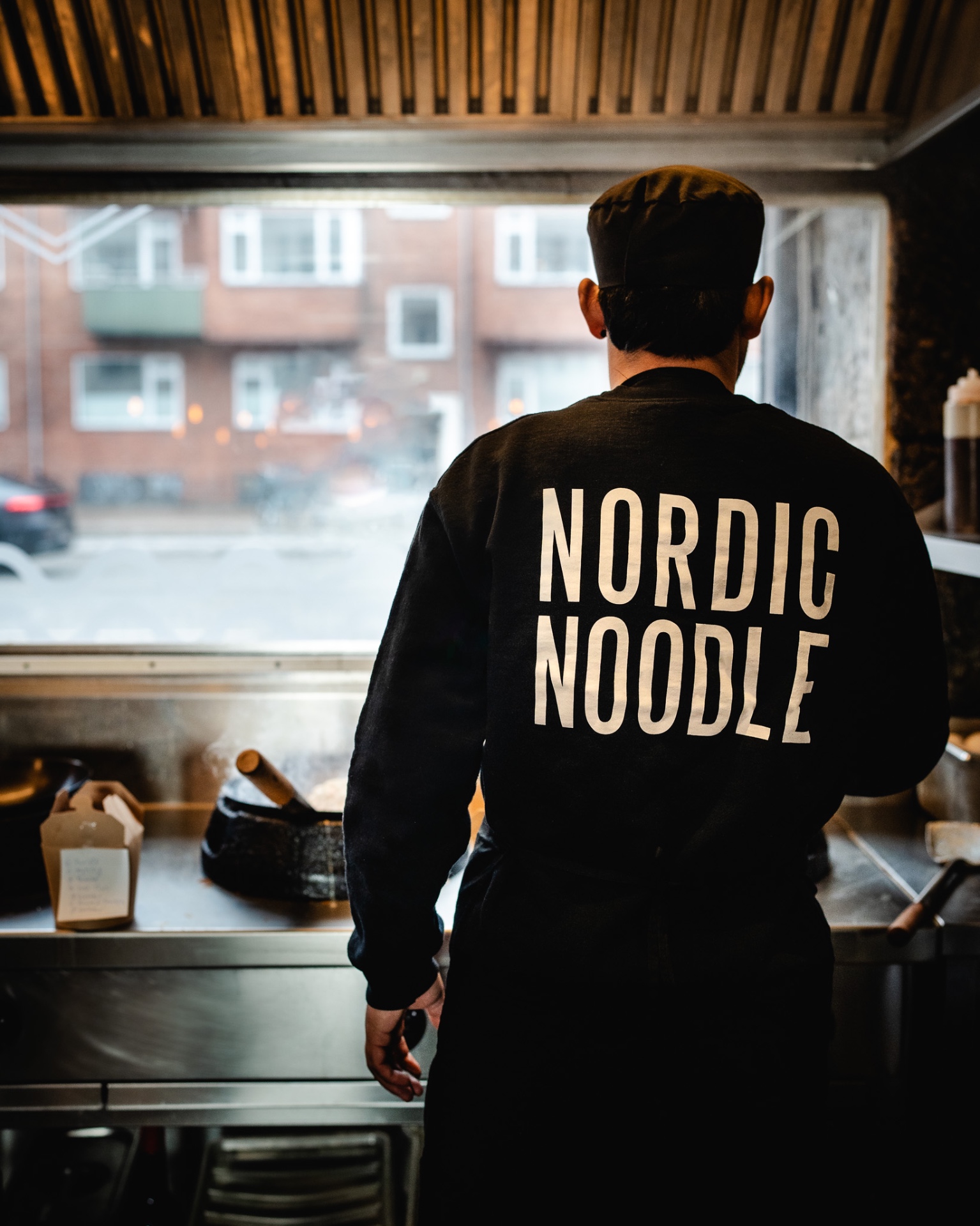 Kok i Nordic Noodle-sweatshirt foran den åbne wok